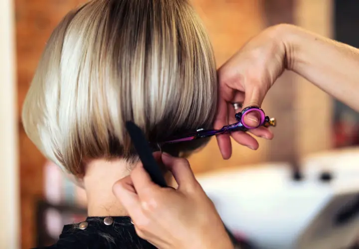Fryzjerka precyzyjnie modeluje prosty bob, używając kolorowych nożyczek.