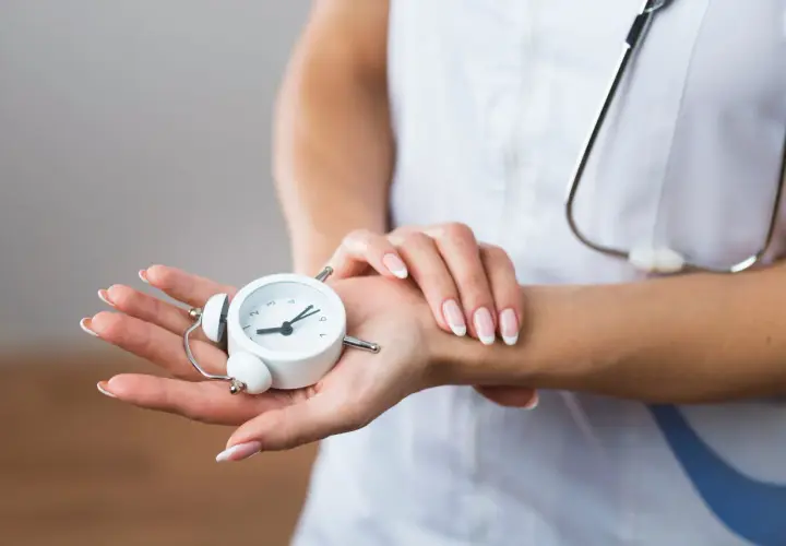Manos de profesional de la salud sostienen un reloj despertador, simbolizando la presión de trabajo y la importancia del tiempo en la atención médica.