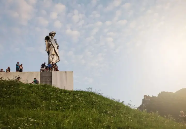 Pomnik Janosika góruje nad wzgórzem, a pod nim siedzą ludzie.