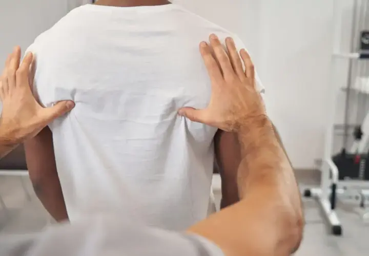 Fizjoterapeuta bada plecy pacjenta, szukając przyczyny bólu w kręgosłupie piersiowym.
