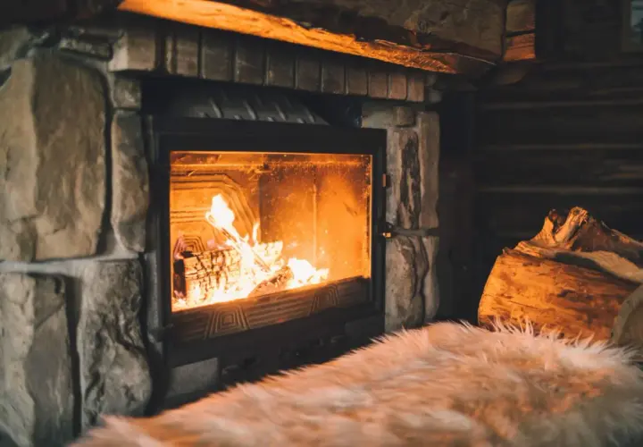Un feu crépite joyeusement dans une cheminée en pierre, réchauffant l'atmosphère d'un chalet rustique. Des bûches attendent patiemment à côté.