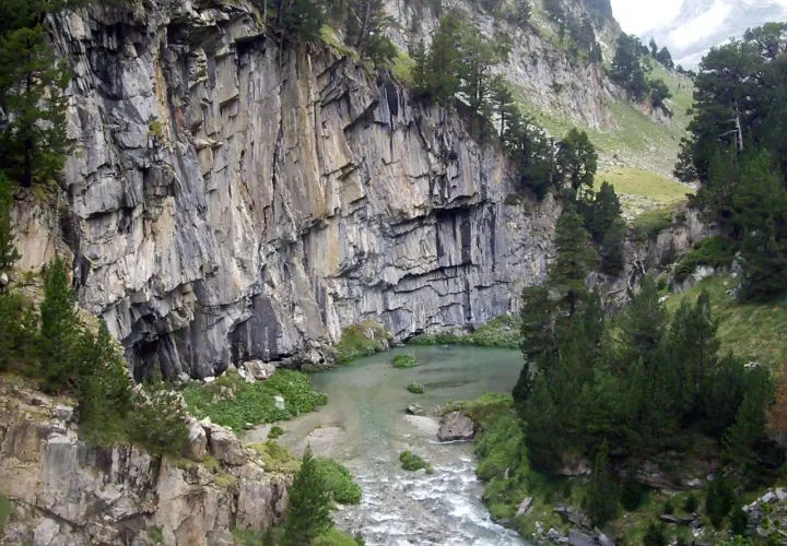 Impresionante pared rocosa junto a un río y vegetación exuberante en el forau de Aigualluts.