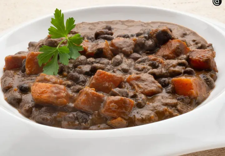 Un plato de frijoles negros con trozos de camote y perejil fresco.