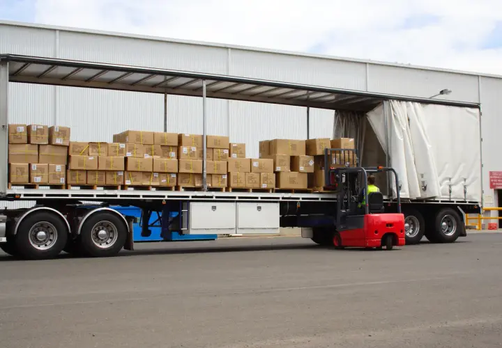 Czerwony wózek widłowy ładuje pudła na naczepę. Taki tir może przewieźć nawet 25 ton ładunku.