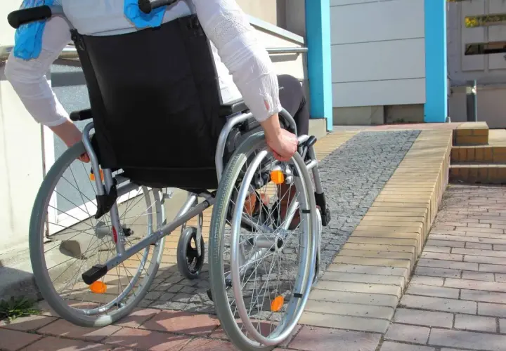Osoba na wózku inwalidzkim wjeżdża na podjazd, pokazując, jak zrobić podjazd dla niepełnosprawnych.