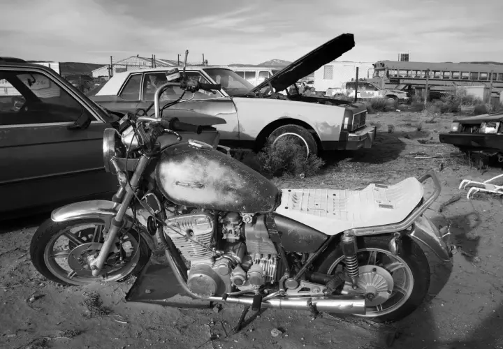 Una moto vieja y un coche en un desguace. ¿Como saber si una moto esta dada de baja? Busca señales de óxido y piezas faltantes.