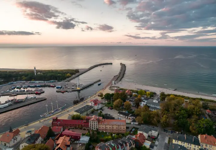 Widok z lotu ptaka na port i plażę w Ustce. Widać łodzie, latarnię morską i budynki. To jedne z wielu ustka atrakcje turystyczne.