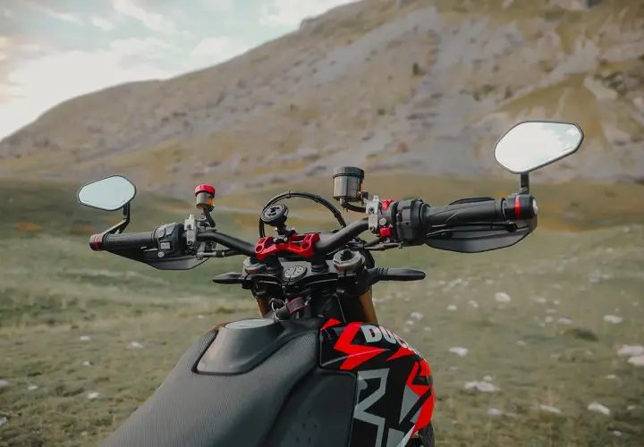 Manubrio di una moto con specchietti bar end, pronto per un'avventura tra le montagne.