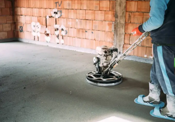 Pracownik wykonuje zacieranie betonu za pomocą mechanicznej zacieraczki.