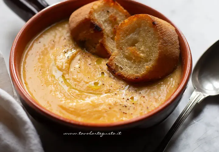 Una ciotola di terracotta contiene una vellutata crema di fagioli cannellini, guarnita con crostini dorati e un filo d'olio.