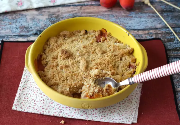 Un délicieux crumble abricot tout juste sorti du four, prêt à être dégusté. La cuillère y a déjà fait un trou.