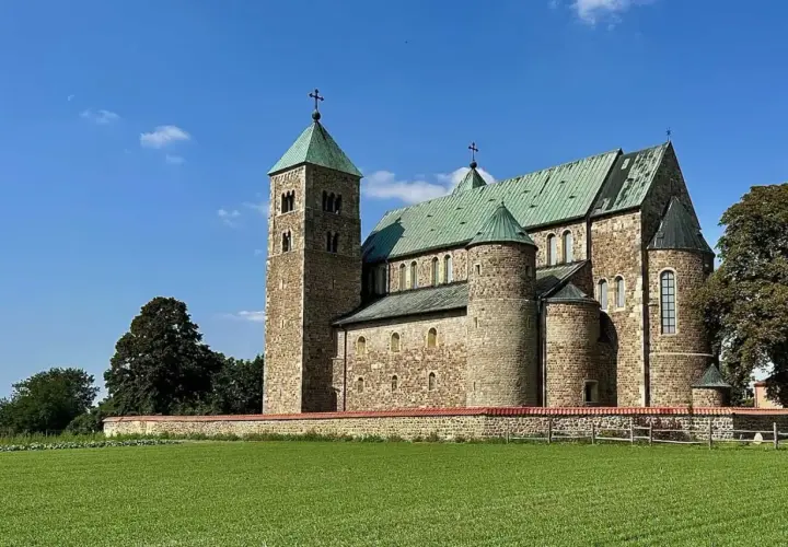 Romańska bazylika tum pod Łęczycą, z zielonymi dachami i kamiennym murem, na tle błękitnego nieba.