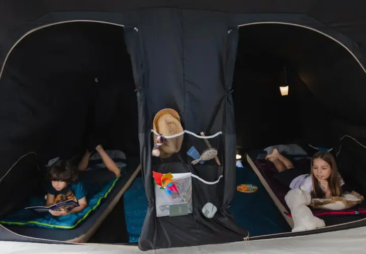 Dzieci cieszą się **campingiem dla dzieci** w namiocie. Chłopiec czyta książkę, dziewczynka bawi się z pluszakiem.