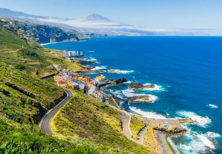 Costa de Tenerife con pueblo colorido, mar azul y el Teide al fondo. ¡Perfecto para tus viajes a Tenerife todo incluido 2x1!