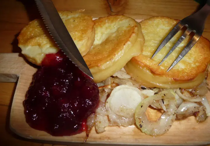 Usmażony oscypek z żurawiną, cebulą i sztućcami na desce.