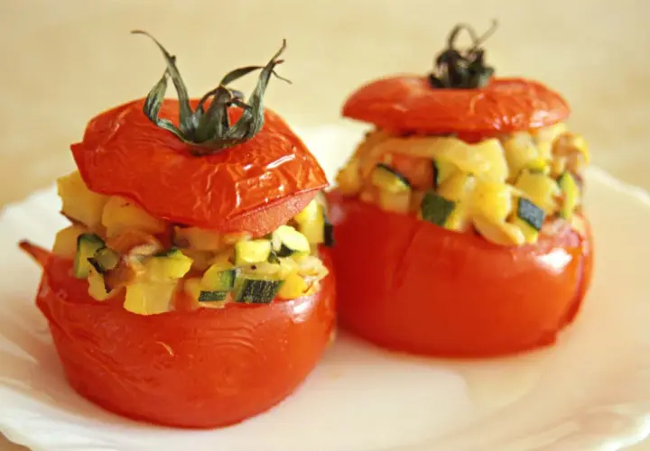 Deux tomates farcies végétariennes garnies de légumes coupés en dés, servies sur une assiette blanche.