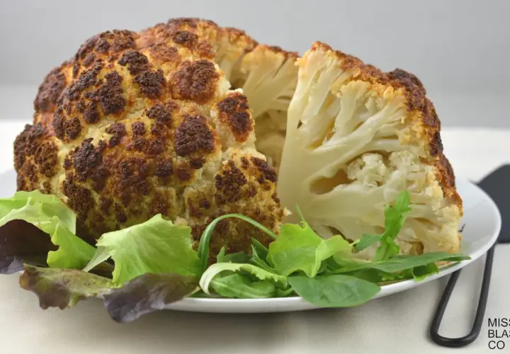 Coliflor al horno, dorada y tierna, servida con una fresca ensalada verde. Un plato saludable y delicioso.