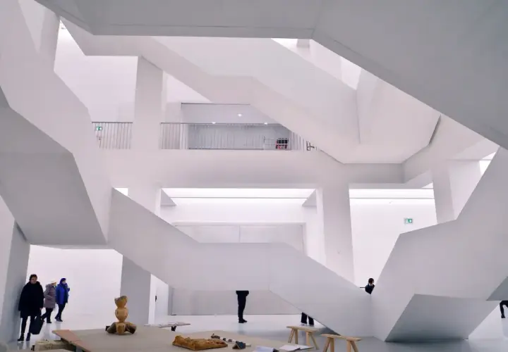 Nowoczesne muzeum sztuki z białymi, geometrycznymi schodami i kilkoma zwiedzającymi.
