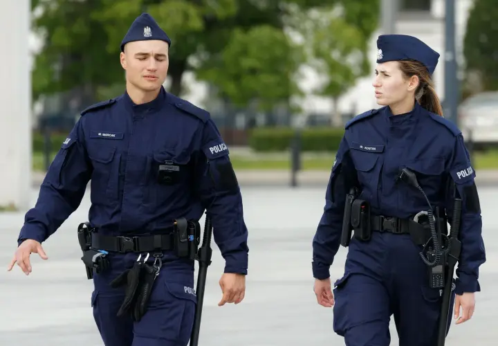 Dwóch policjantów w granatowych mundurach, z widocznymi stopniami w policji, patroluje teren.