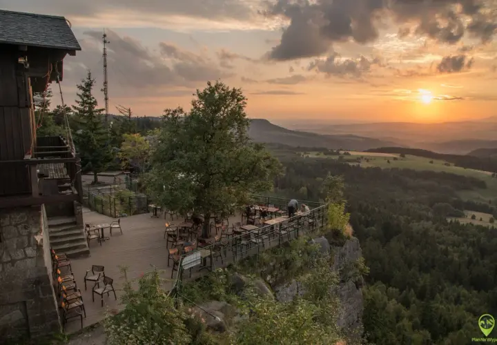 Widok z tarasu restauracji na Górach Stołowych o zachodzie słońca. Drewniany taras z meblami, otoczony skalistym zboczem i lasem.