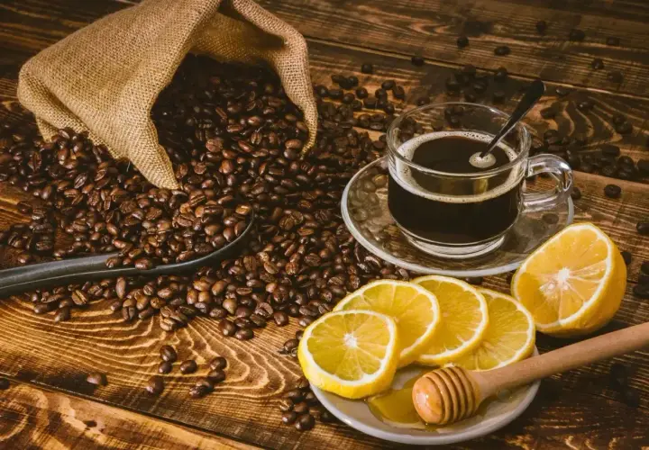 Aromatyczna kawa z cytryną i miodem, otoczona ziarnami kawy wysypującymi się z worka.