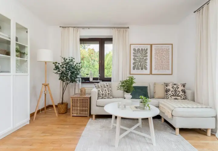 Przytulny salon, idealne **mieszkanie dla młodych**. Jasna sofa, stolik kawowy, rośliny i botaniczne plakaty tworzą relaksującą atmosferę.