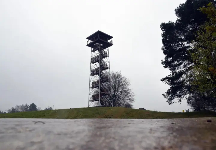 Wieża widokowa na górze lemana, z krętymi schodami i drewnianymi platformami, góruje nad zielonym wzgórzem.