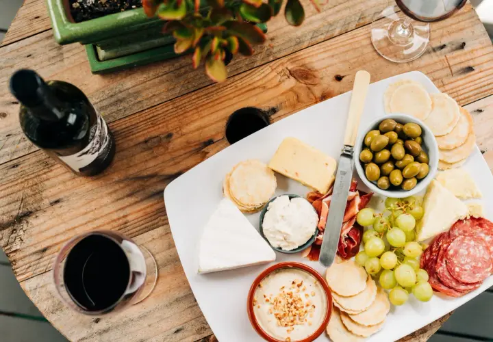 Un plateau de fromages variés, charcuterie, olives et raisins, accompagné d'une bouteille et d'un verre de vin rouge. Quel vin rouge avec un plateau de fromage varié ?
