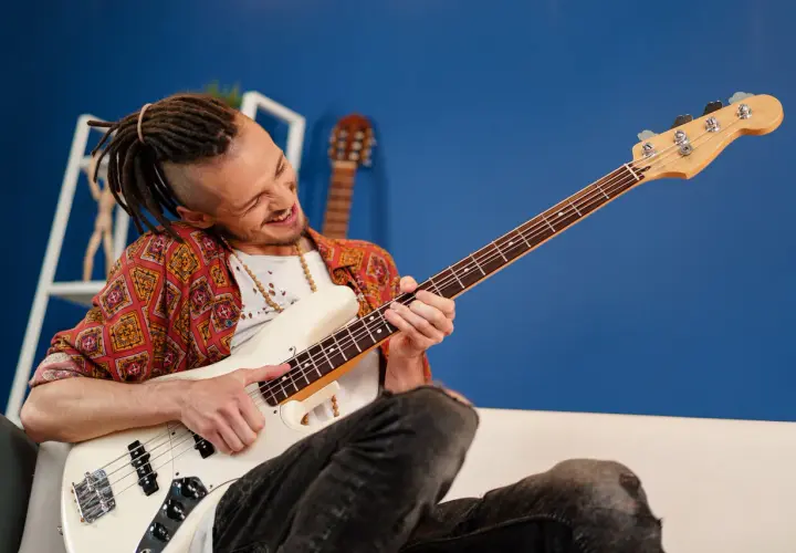 Mężczyzna z dredami gra na białej gitarze basowej. Ile strun ma gitara basowa? Ta ma cztery.