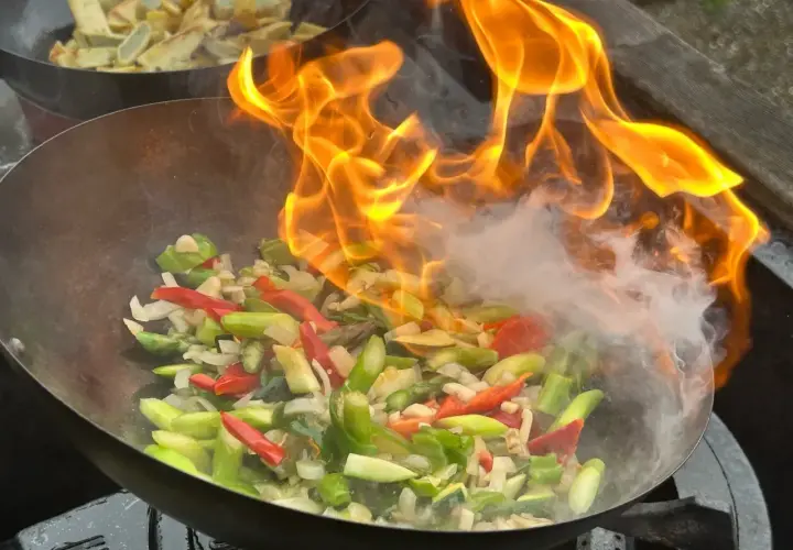 Ogień buchający z woka podczas przygotowywania pysznego stir fry z warzywami.