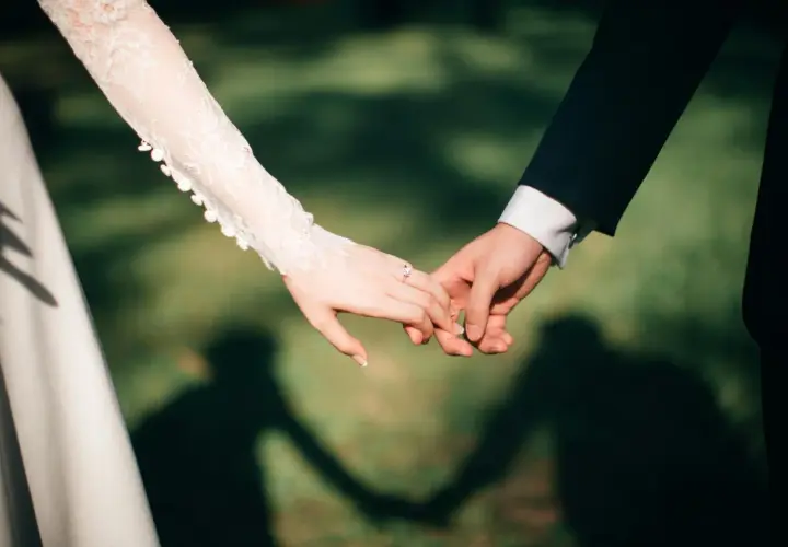 Dłonie nowożeńców splecione w uścisku, symbolizującym przysięgę małżeńską. Na palcu panny młodej lśni pierścionek.