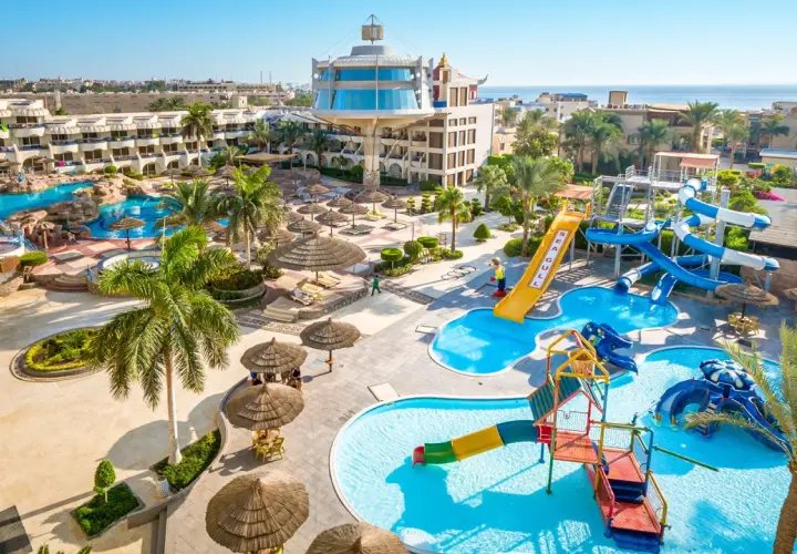 Resort Seagull z basenami i zjeżdżalniami wodnymi, otoczony palmami i budynkami hotelowymi, blisko morza.