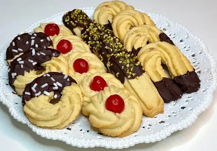 Vassoio di frolla montata: biscotti decorati con cioccolato, granella di pistacchio e ciliegie candite.