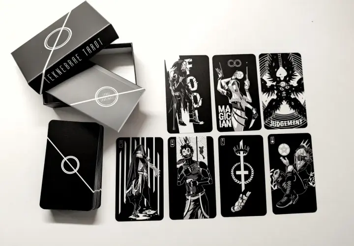 Czarno-białe karty z talii tarot z 5 kartami, w tym Mag, Sąd i inne postacie. Pudełko z napisem "TEKNEBRAE TAROT".