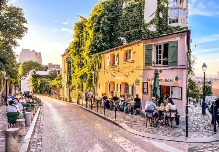 Ulica na Montmartre, z kawiarnią La Maison Rose i ludźmi siedzącymi przy stolikach.