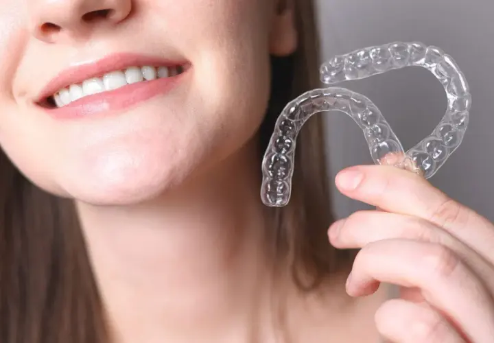 Una persona sonríe mostrando sus dientes y sostiene un alineador transparente. Invisalign para que sirve: para corregir la alineación dental de forma discreta.