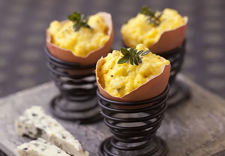 Une entrée pour Pâques avec des œufs farcis, garnie d'herbes fraîches. Du fromage bleu est disposé à côté.