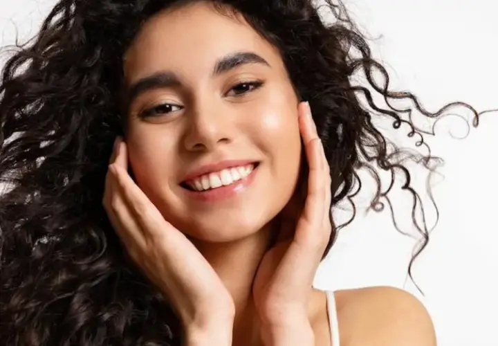 Sonrisa radiante con un toque de strawberry makeup, cabello rizado oscuro y piel luminosa.