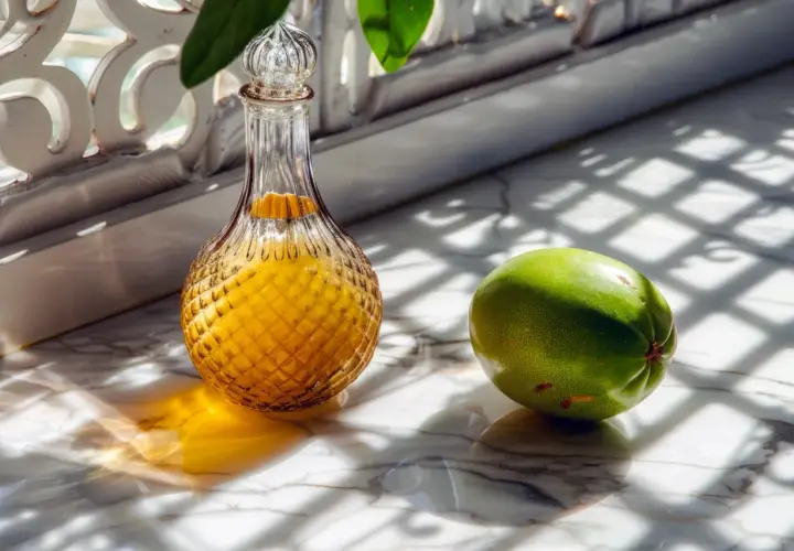 Bouteille de rhum arrangé mangue, à côté d'un fruit vert sur un marbre lumineux.