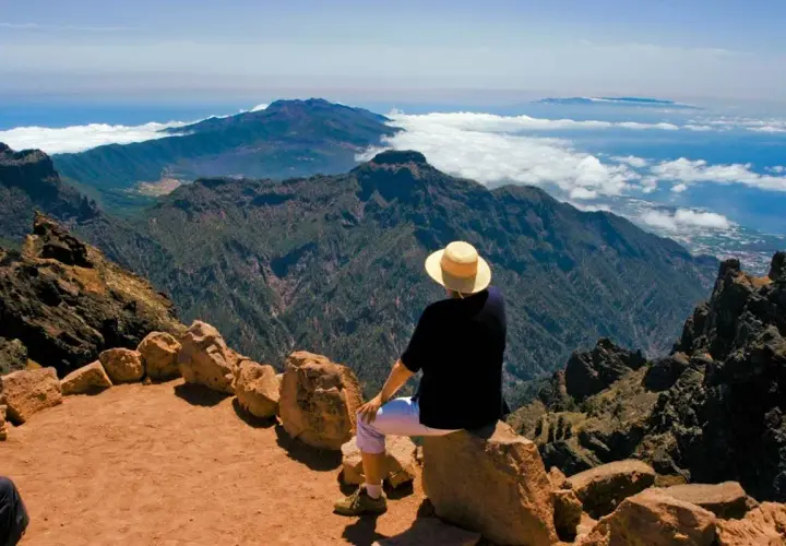 Persona con sombrero admira el paisaje montañoso y el mar, disfrutando de las **rutas La Palma**.