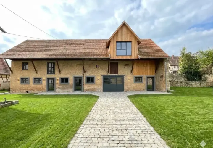 Belle grange rénovée avec une extension en bois. Le chemin pavé mène à la porte de garage. Le prix de la rénovation de grange est justifié par ce résultat.