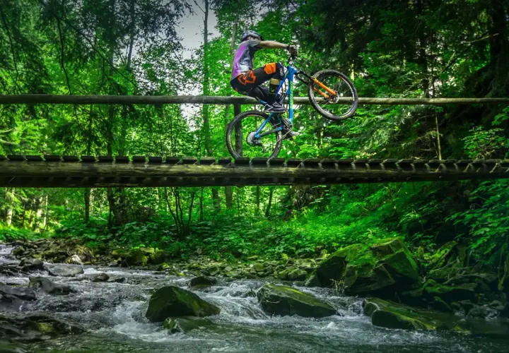 Rowerzysta wykonuje trik na drewnianym moście nad potokiem. Wspaniałe **trasy rowerowe Zakopane** czekają na odkrycie!