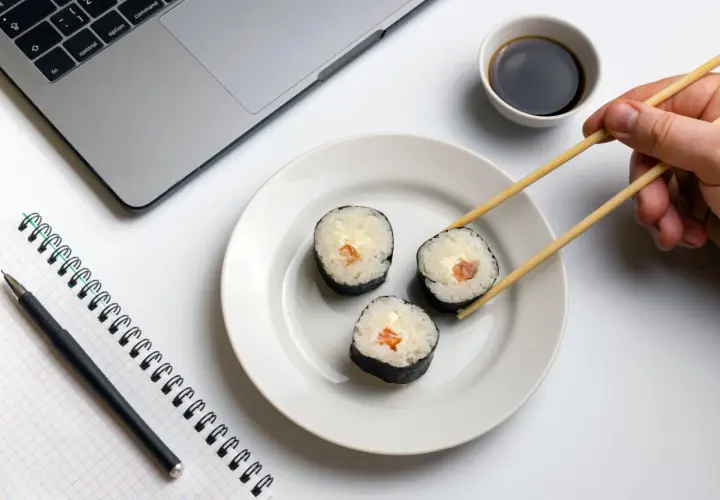 Praca i zdrowie idą w parze. Na biurku laptop, notatnik i pałeczki do sushi, idealne dla zwolenników peskatarianizmu.