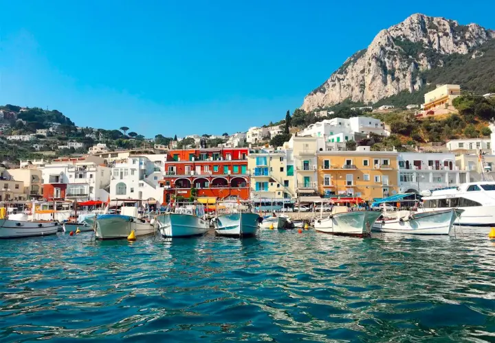 Vue du port de Capri, avec des bateaux blancs amarrés et des maisons colorées à flanc de colline. Un paysage typique de Capri, pas Ischia.