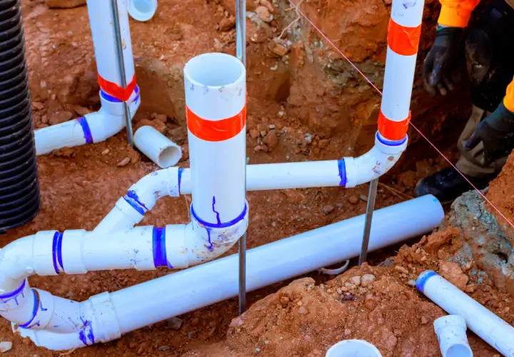 Prace hydrauliczne w toku: łączenie rur pcv w wykopie. Widać fragmenty instalacji kanalizacyjnej i drenażowej.
