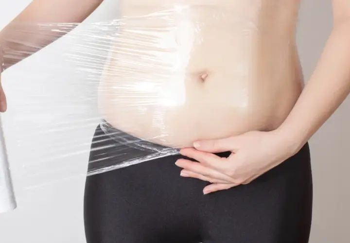 Osoba owija brzuch folią spożywczą, próbując dowiedzieć się, body wrapping co to jest i jak działa.