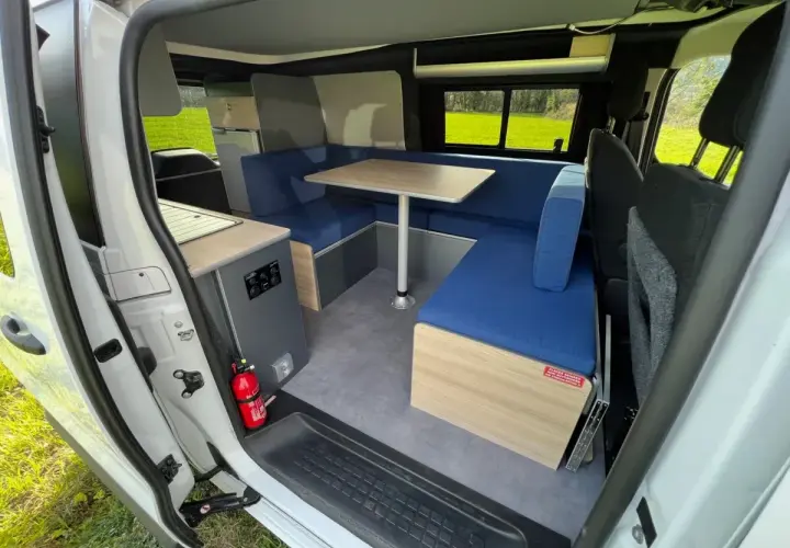 Aménagement intérieur d'un camping-car : banquettes bleues, table, coin cuisine. Idéal pour construire son camping car.