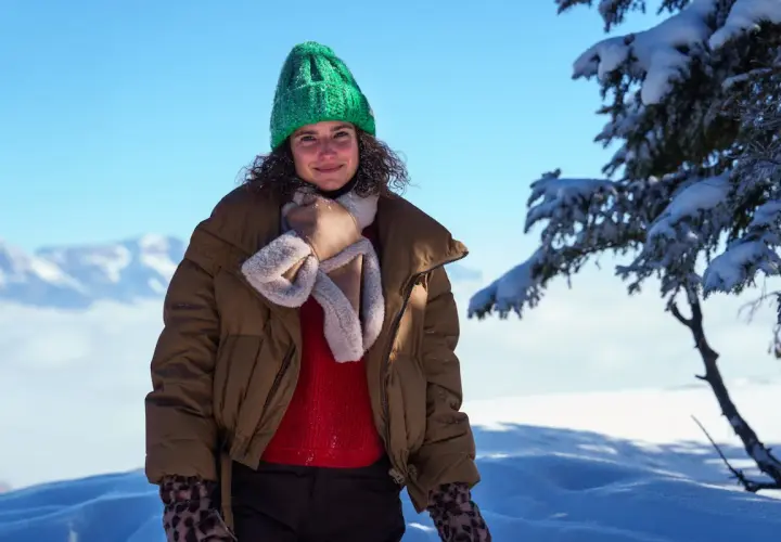 Frau mit grüner Strickmütze und brauner Winterjacke im Schnee.