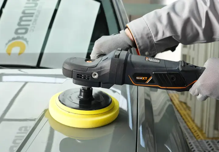 Persona con guantes usa una pulidora para detallar el capó de un coche gris.