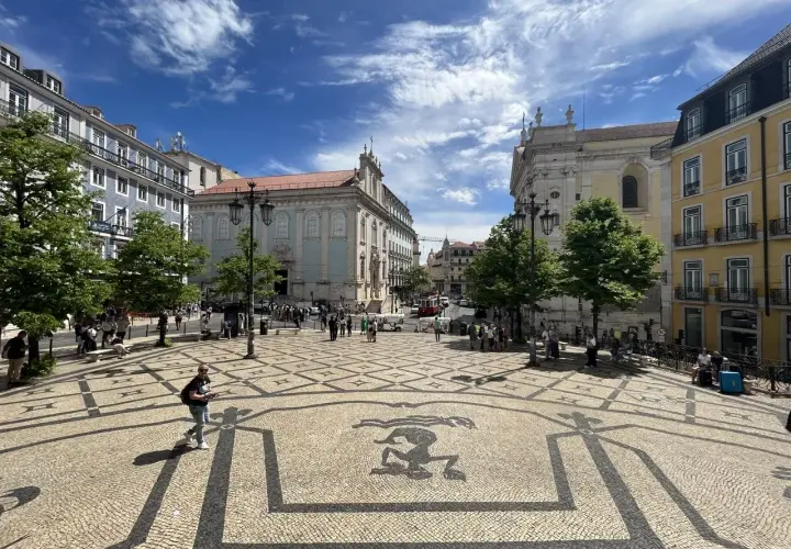 A sunny day trip to Lisbon, exploring a beautiful square with intricate mosaic paving and historic buildings under a blue, cloudy sky.
